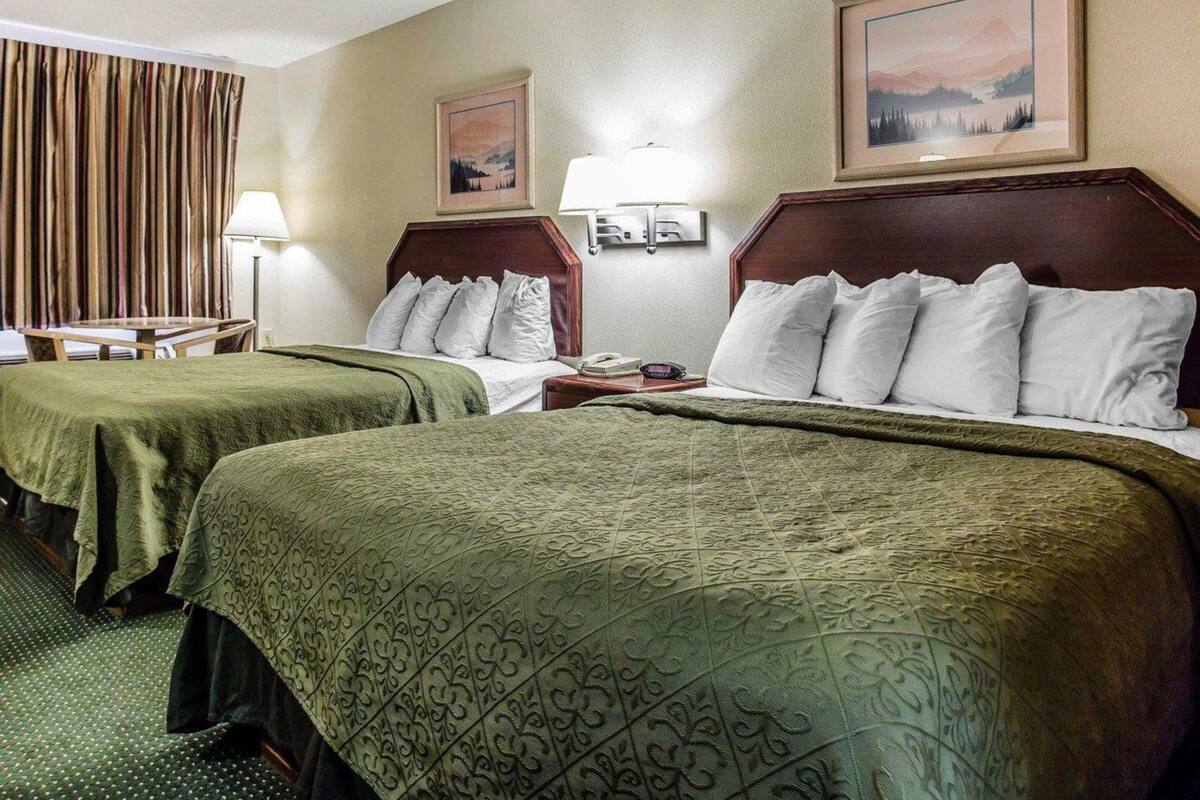 A hotel room with two beds, a desk, a chair, a lamp, and a painting on the wall.