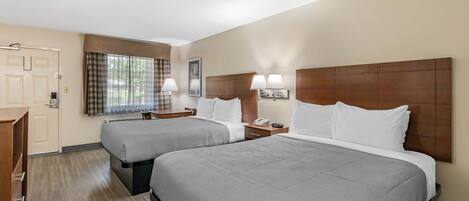 A hotel room with two beds, a desk, a chair, a window with curtains, and a wooden headboard.