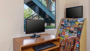 A desk with a computer monitor, keyboard, and a chair. A window reveals a staircase and greenery outside. - Quality Inn & Suites Stockbridge Atlanta South I-75 (Stockbridge)