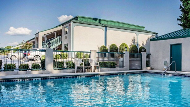 A swimming pool with a white building in the background, a fenced area, and a green-roofed structure to the right. - Quality Inn & Suites Stockbridge Atlanta South I-75 (Stockbridge)