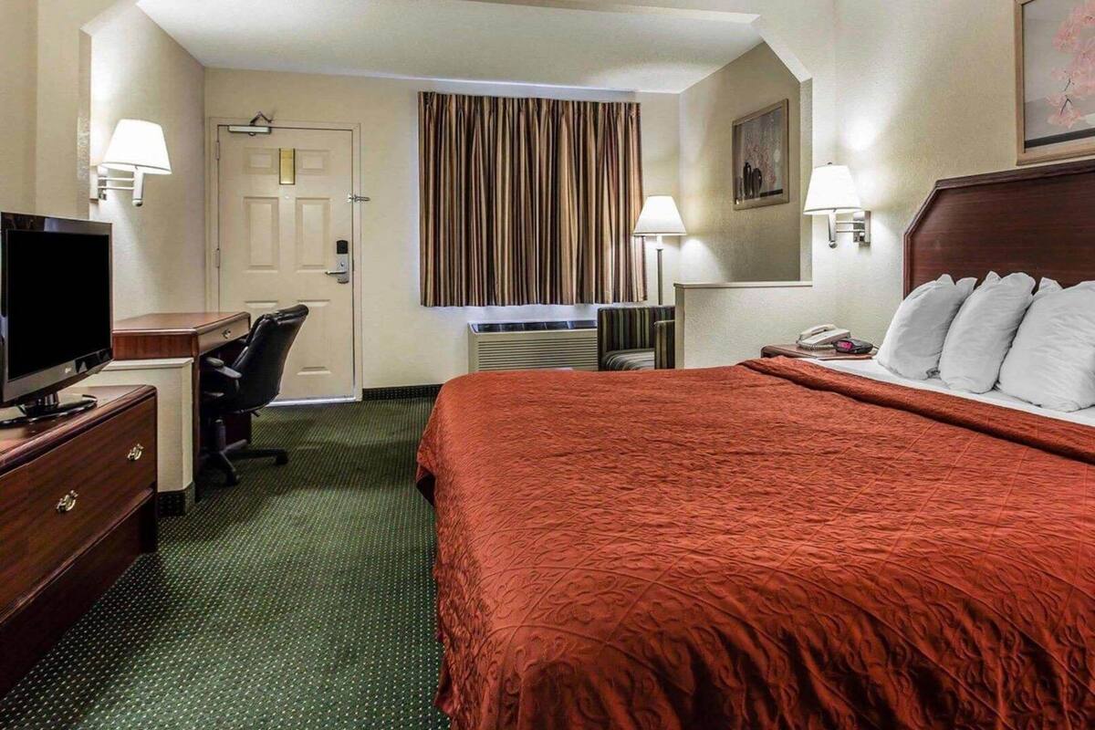 A hotel room with a bed, desk, chair, television, and two lamps.