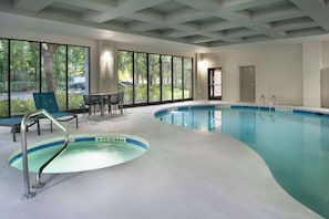 An indoor swimming pool with clear glass walls, a pool ladder, and a seating area with chairs and a table.