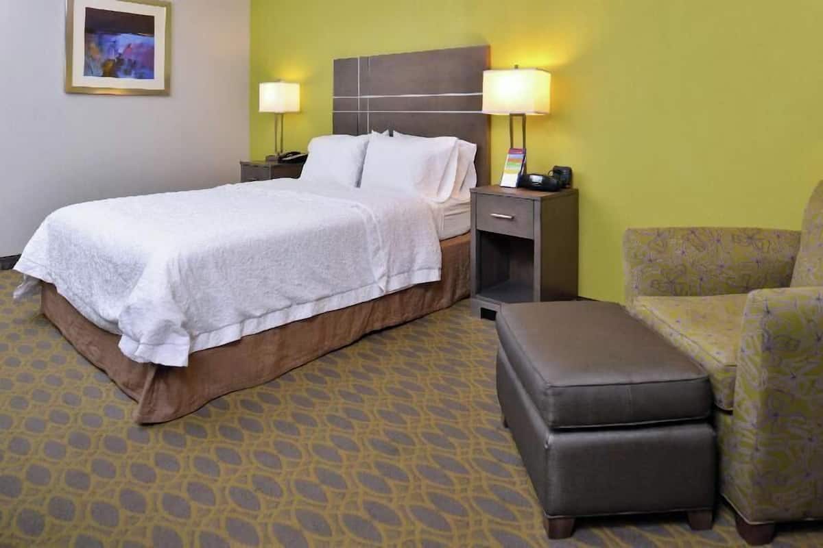 A hotel room with a bed, bedside tables, a chair, and a patterned carpet.