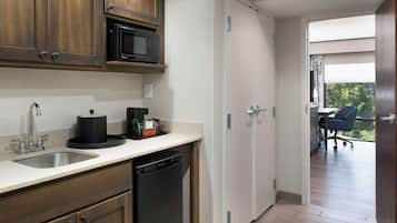 A modern kitchen with a dishwasher, a microwave, and a coffee maker on the counter. There is a door leading to a balcony with a chair.