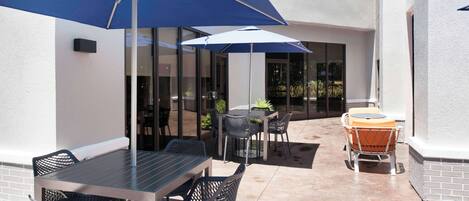 An outdoor patio with a table and chairs, a blue umbrella, and a round table with a cushioned seat.