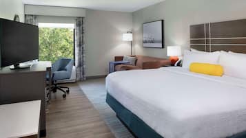 A hotel room with a bed, a desk with a TV, a chair, a sofa, and a window with curtains.