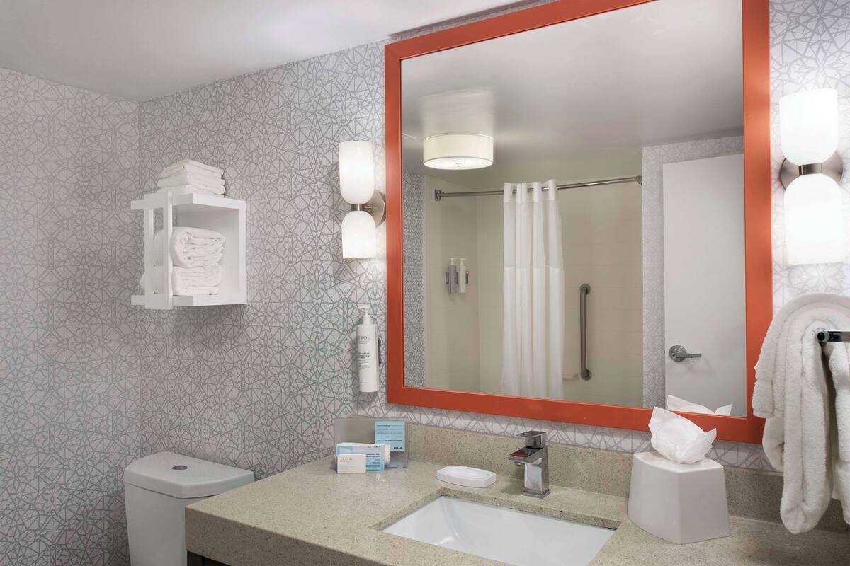Une salle de bain avec un grand miroir, un lavabo, des toilettes et un porte-serviettes.