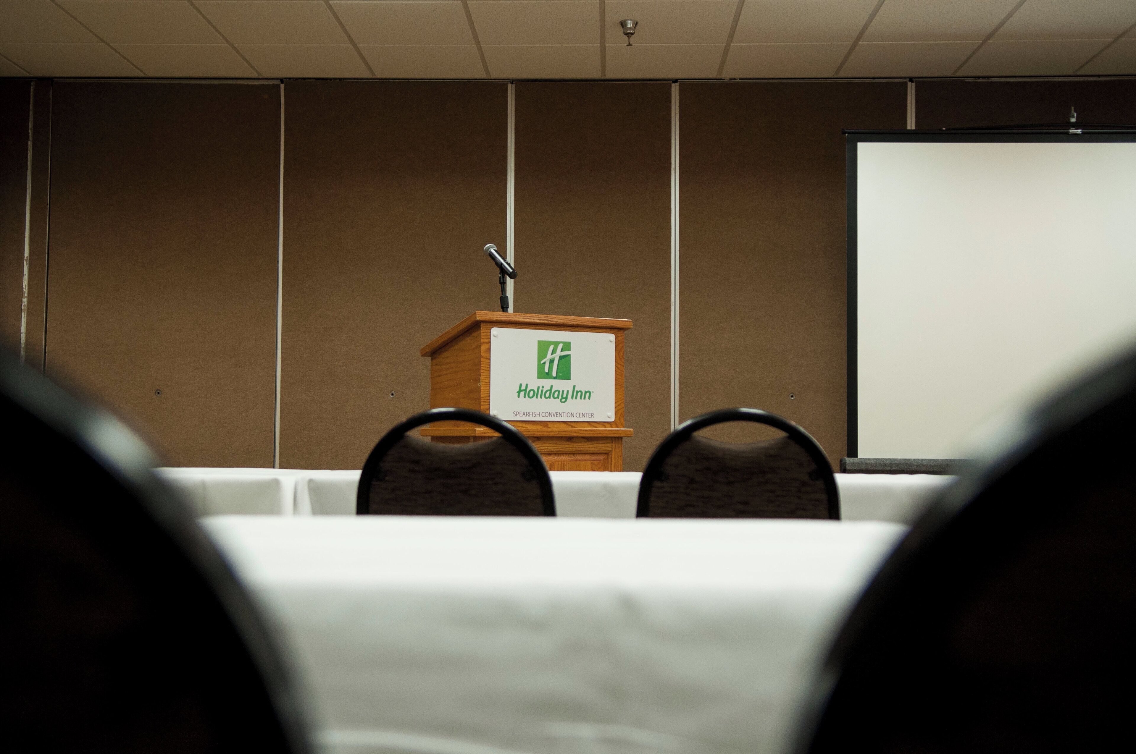 Une salle de conférence équipée d’un pupitre portant l’inscription « Holiday Inn » et d’un écran de projection.