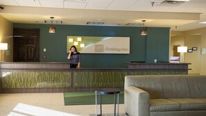 A hotel reception desk with a receptionist, a reception area with a green wall, and a reception desk with a Holiday Inn logo. - Holiday Inn Spearfish - Convention Center by IHG (Spearfish)