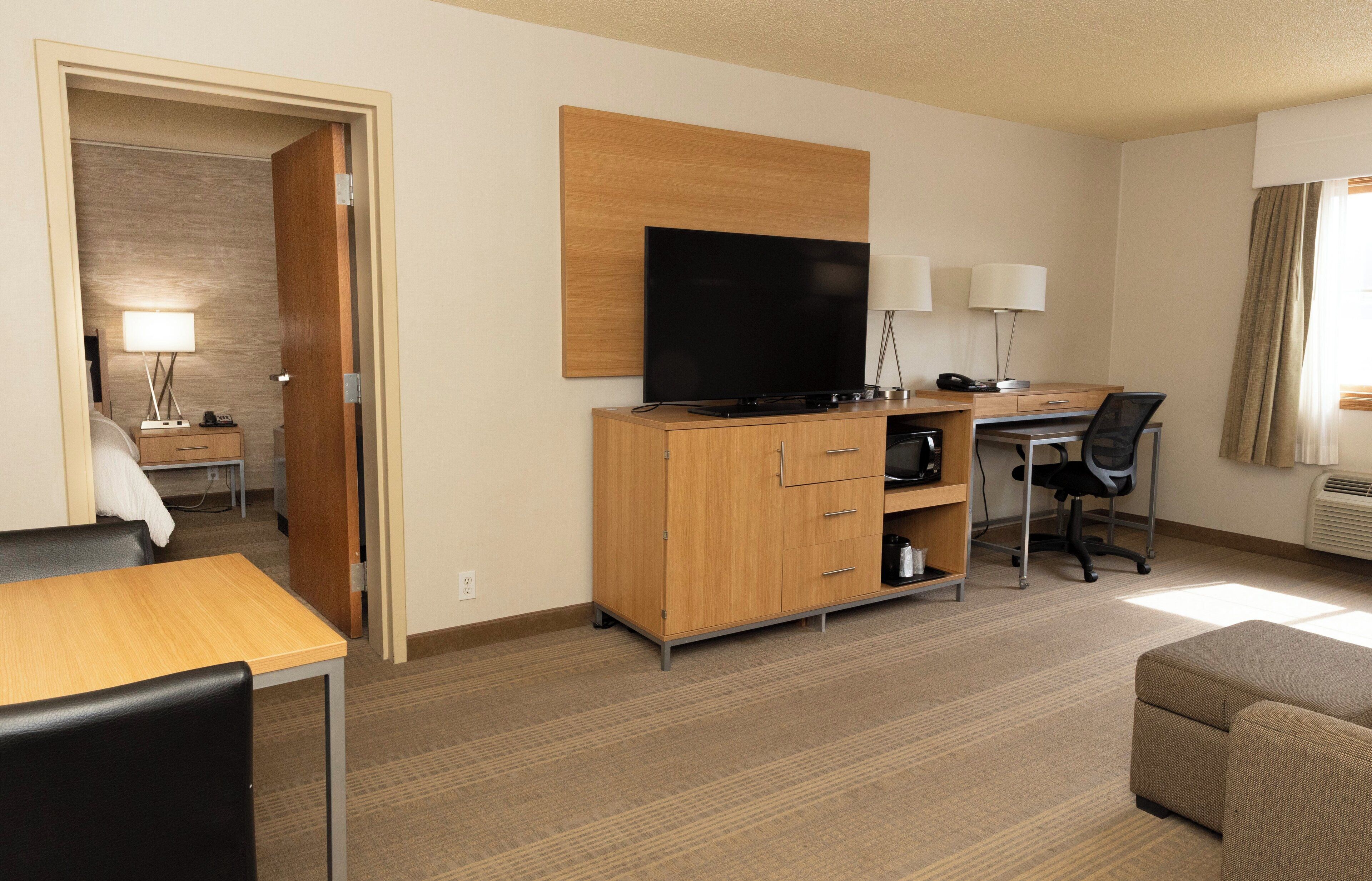 A hotel room with a wooden desk, a television, a sofa, and a lamp.