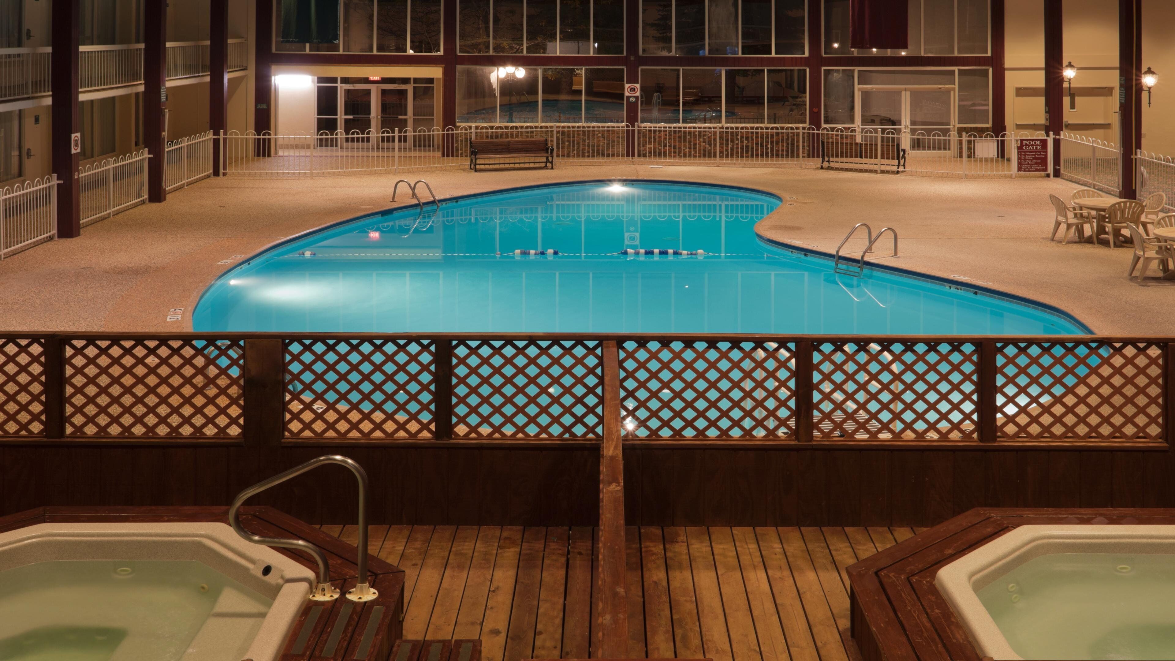 A swimming pool with a wooden deck and lounge chairs, surrounded by a white fence.