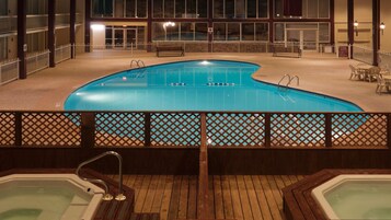 Una piscina con muelle de madera y sillas de descanso, rodeada por una valla blanca.