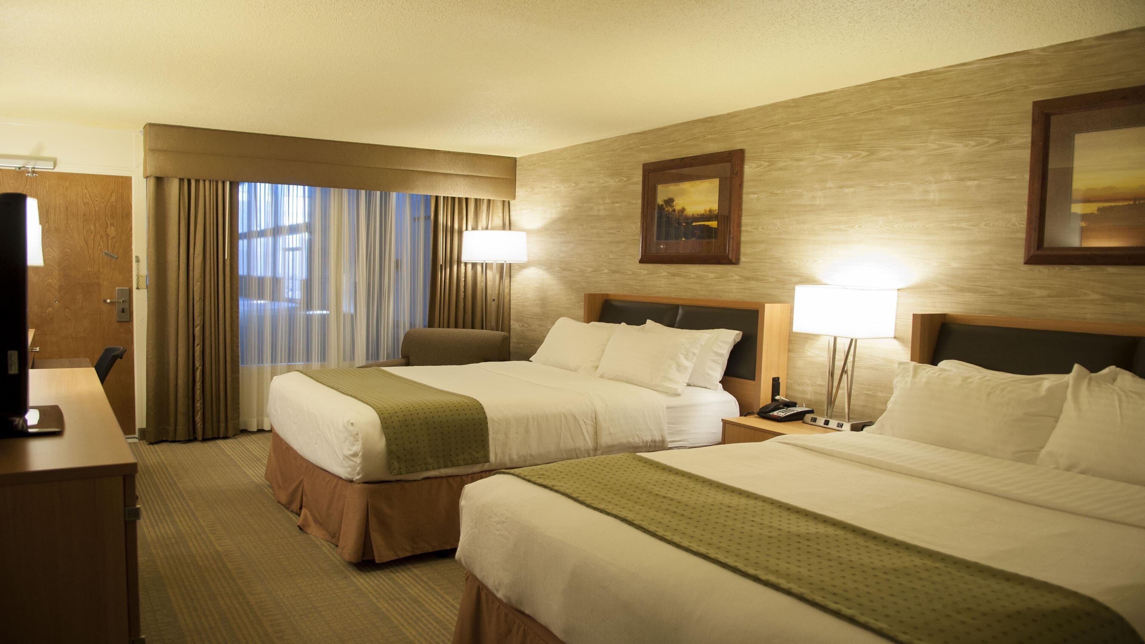 A hotel room with two beds, a desk, a chair, a TV, and a window with curtains.