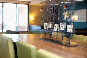 A hotel dining area with a wooden table, green cushioned chairs, and a decorative metal centerpiece. - Holiday Inn Spearfish - Convention Center by IHG (Spearfish)