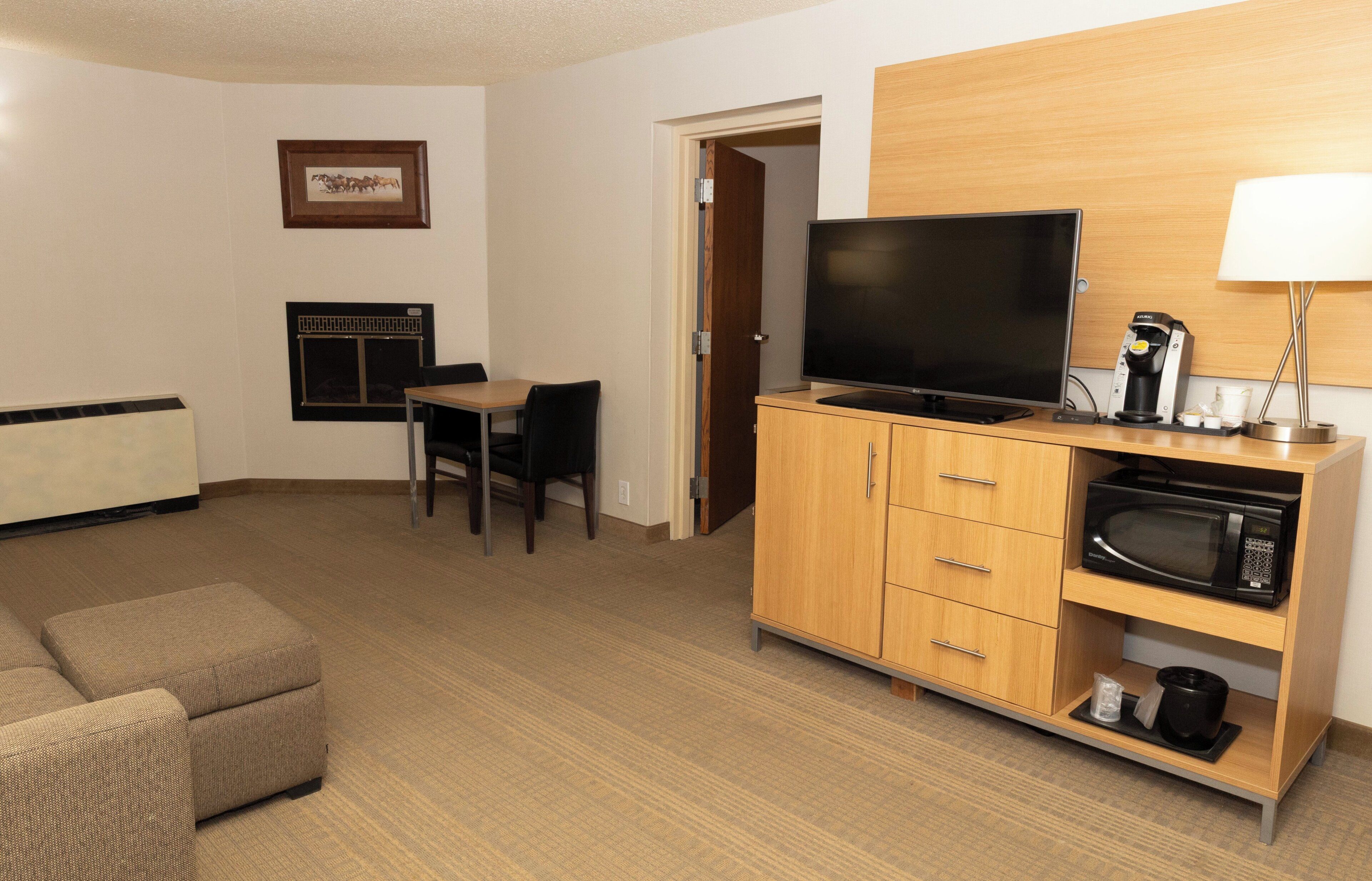 A hotel room with a sofa, a television on a wooden cabinet, a microwave, a coffee maker, and a framed picture on the wall.