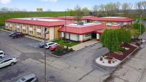 Ein Motel mit rotem Dach und beigen Wänden, mit einem Parkplatz und mehreren Autos.