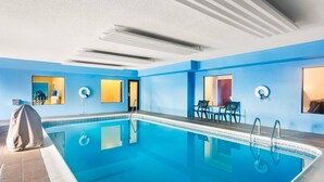 Una piscina con agua azul cristalina, un área de descanso cubierta e iluminación empotrada en el techo.