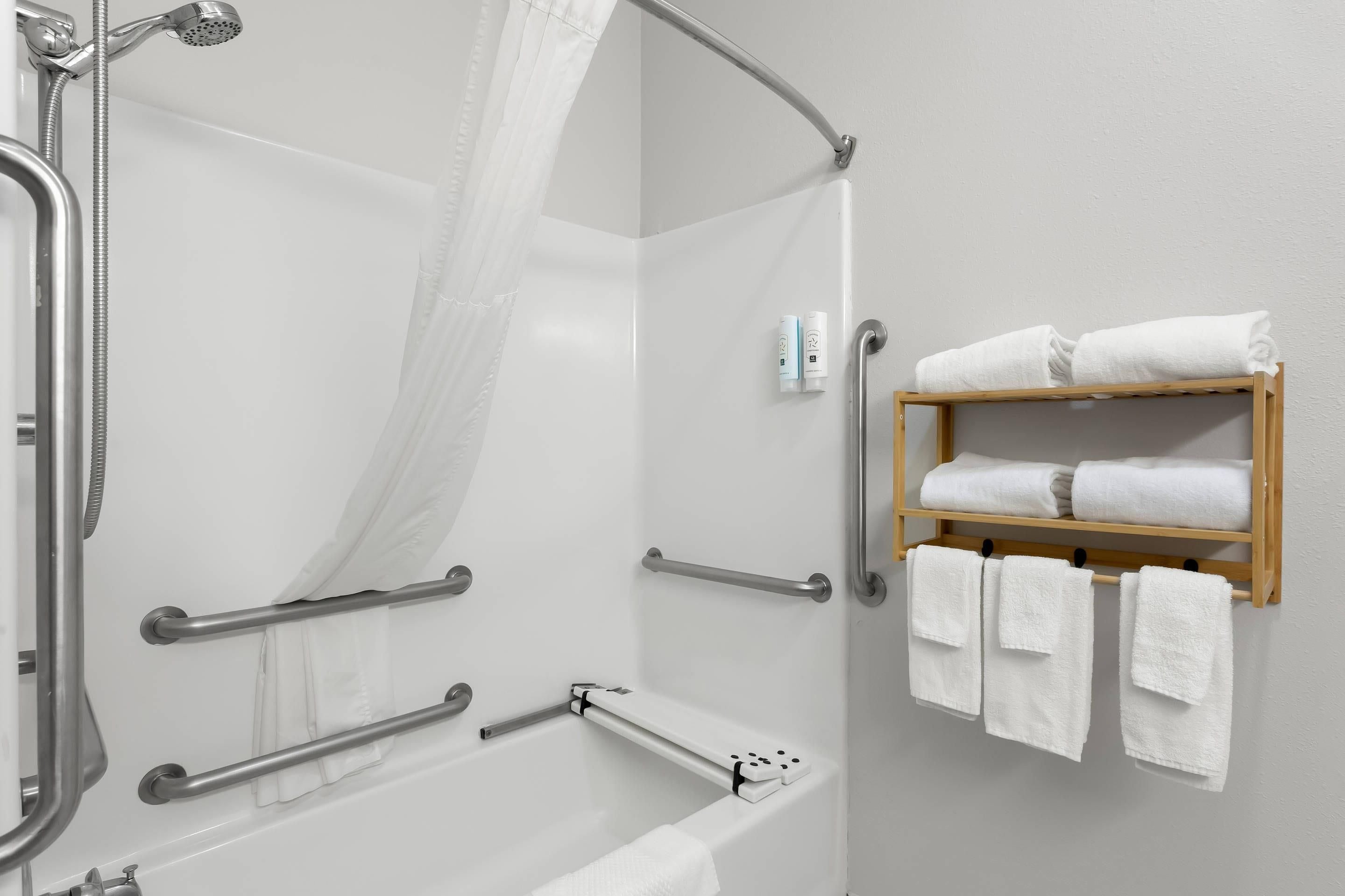 Un baño moderno con ducha, barras de apoyo, bañera y un perchero para toallas.
