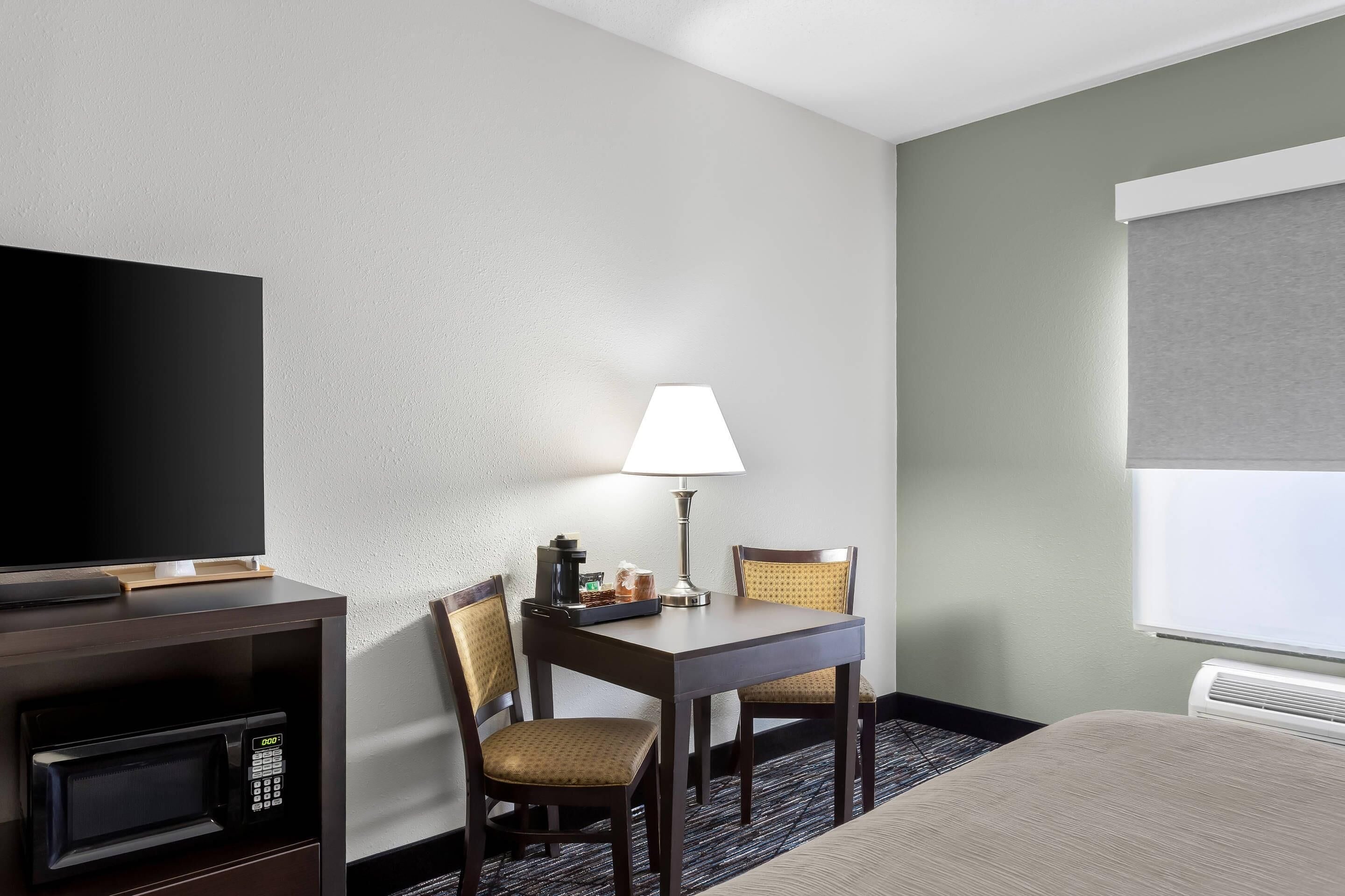 A hotel room with a TV, a table with chairs, a lamp, and a bed.