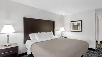 A hotel room with a large bed, two bedside tables with lamps, a nightstand, and a framed picture on the wall.