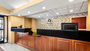 Zona de recepción de hotel con un mostrador de madera, una encimera negra y una pared de mosaicos.