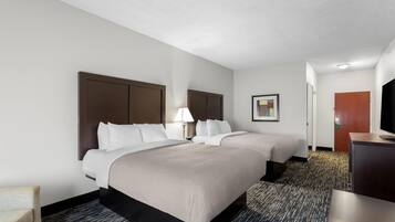 A hotel room with two beds, a desk, a chair, and a carpeted floor.