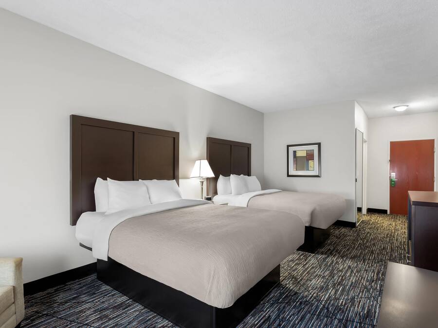 A hotel room with two beds, a desk, a chair, and a carpeted floor.
