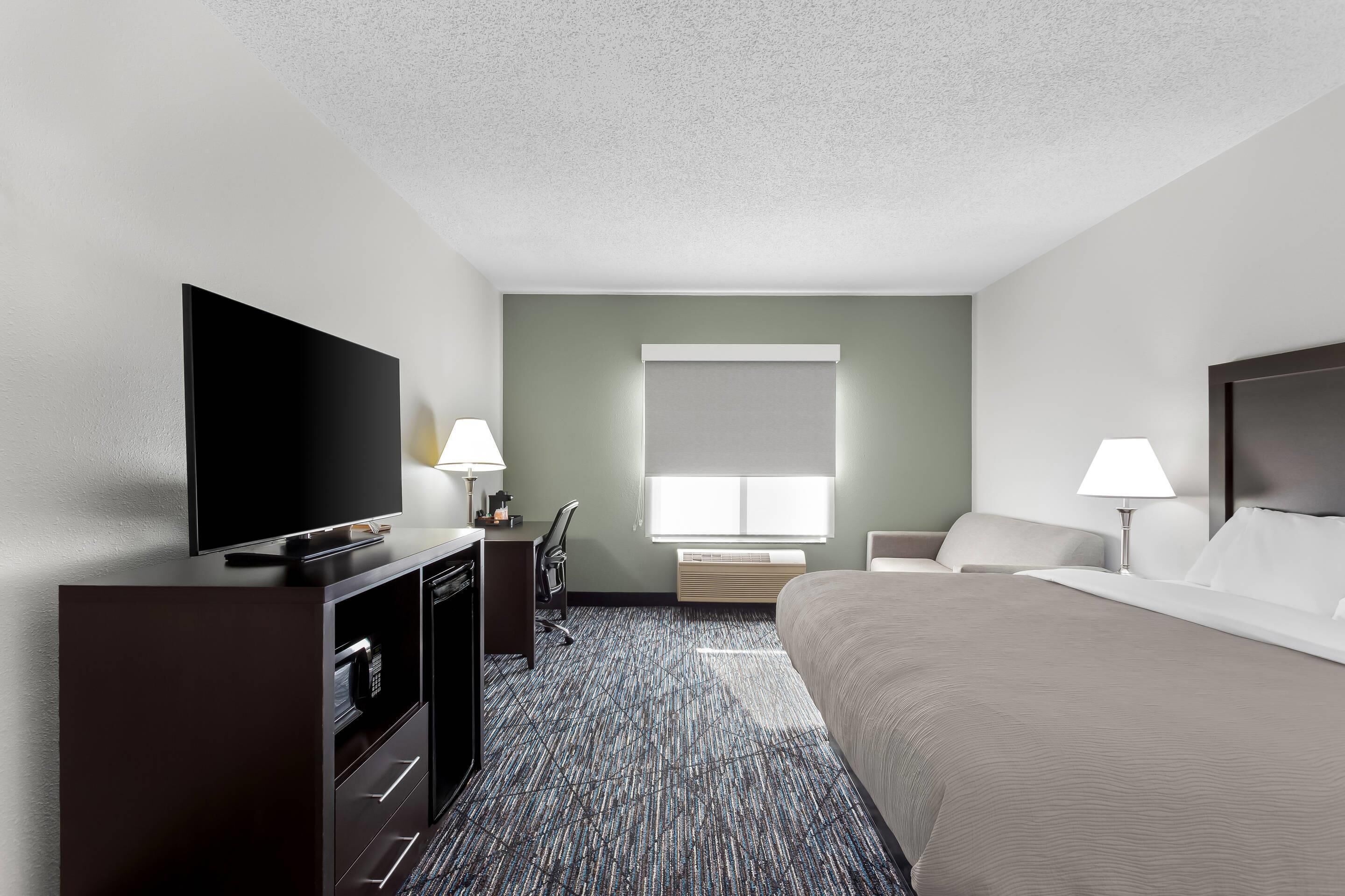 A hotel room with a bed, a TV, a desk, and a window.