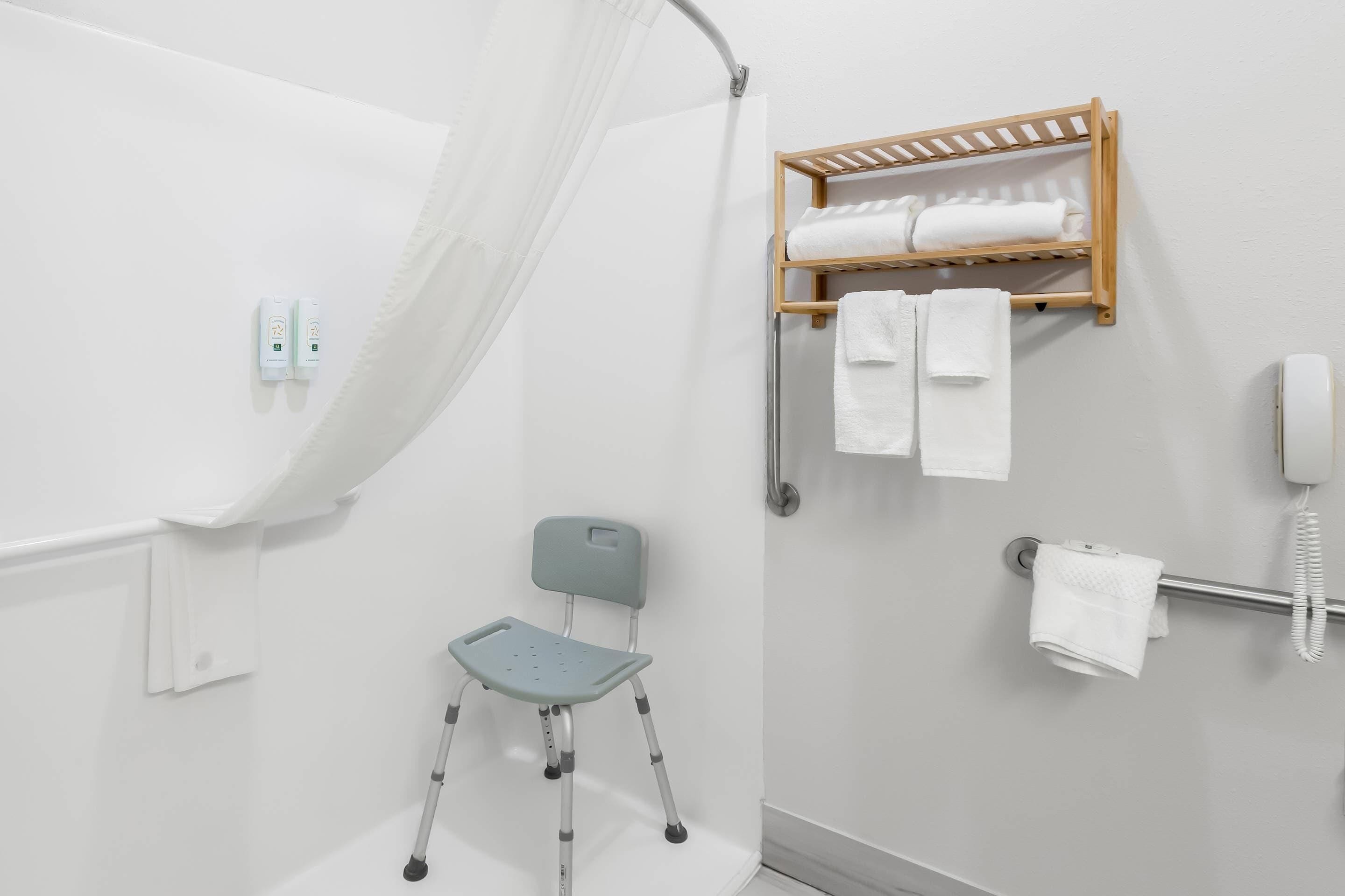 A bathroom with a shower, a chair, a towel rack, and a phone.
