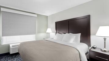 Habitación de hotel con una cama grande, una mesita de noche con lámpara, una ventana con persiana y un calentador de pared.