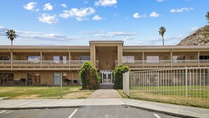 A two-story building with a central entrance, balconies, and a fenced parking area.