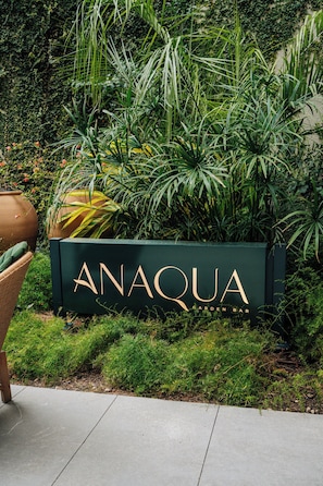 A sign for ANAQUA GARDEN BAR surrounded by lush greenery.