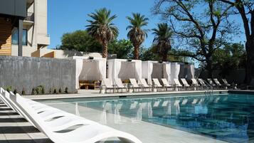Piscina com espreguiçadeiras brancas e palmeiras ao fundo.