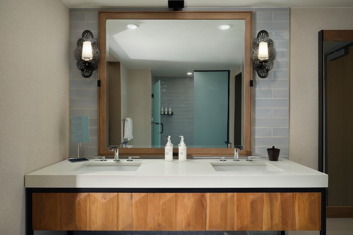 A modern bathroom with two sinks, a large mirror, and wall-mounted sconces.
