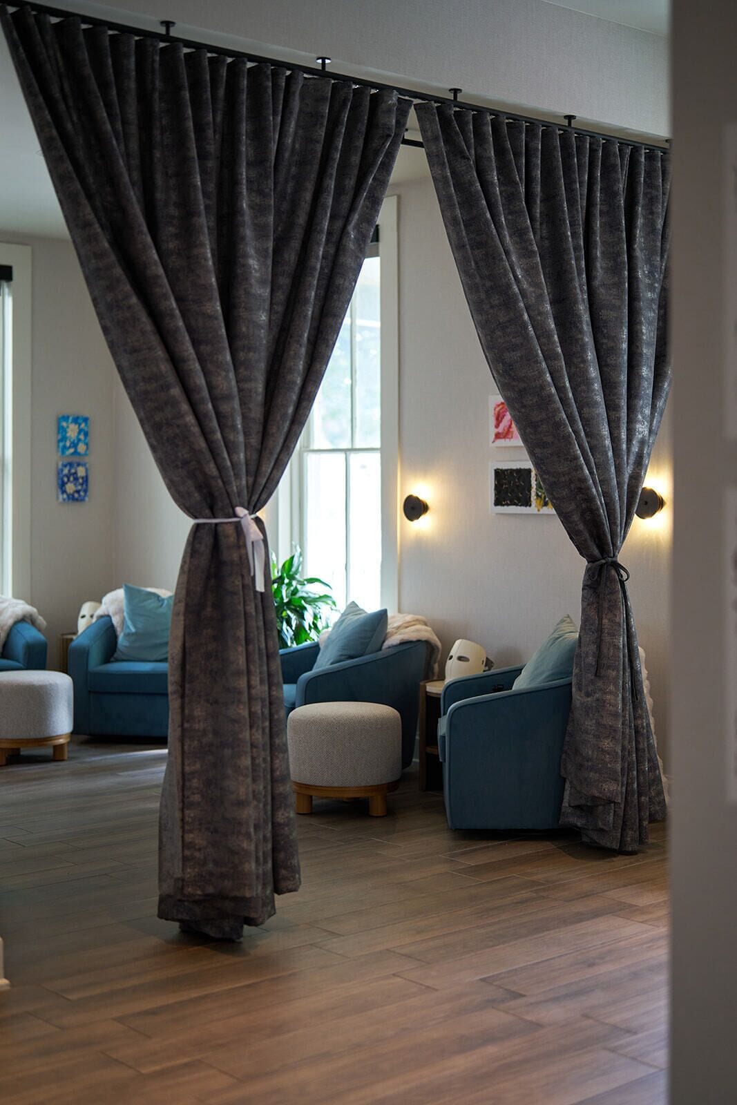 A living room with two blue armchairs, a grey ottoman, and a dark grey curtain.