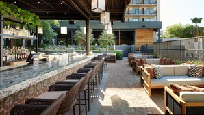 Un área de bar al aire libre con una barra larga, sillas de mimbre y una zona de estar con sofás.