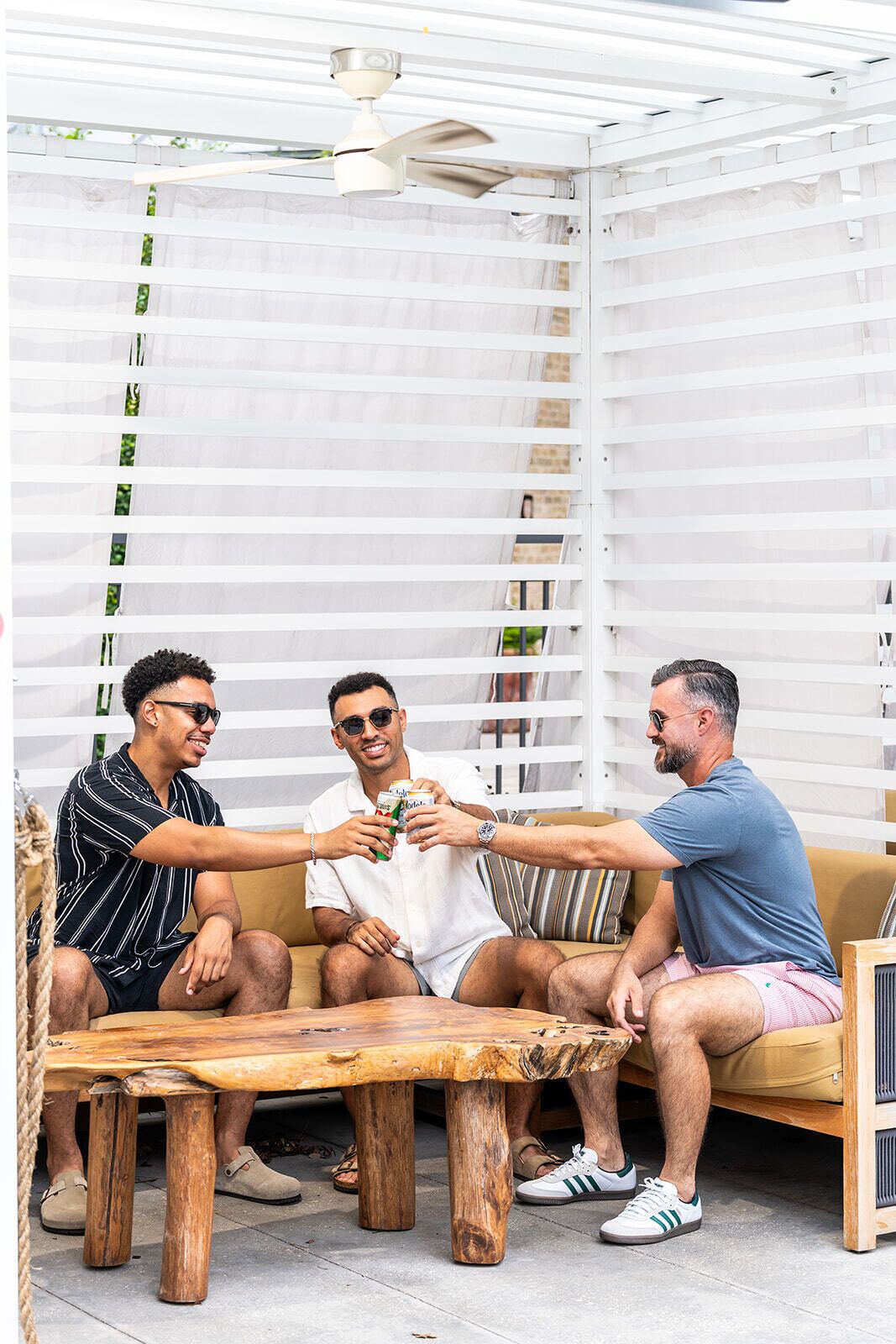 A group of people seated around a wooden table in a covered outdoor area with white railings and a ceiling fan.
