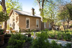 Una casa de ladrillo con chimenea, rodeada de abundante vegetación y un pequeño jardín.