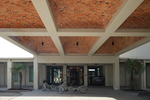 Entrada de un edificio con techo de ladrillo, dos palmeras y bicicletas estacionadas en frente.