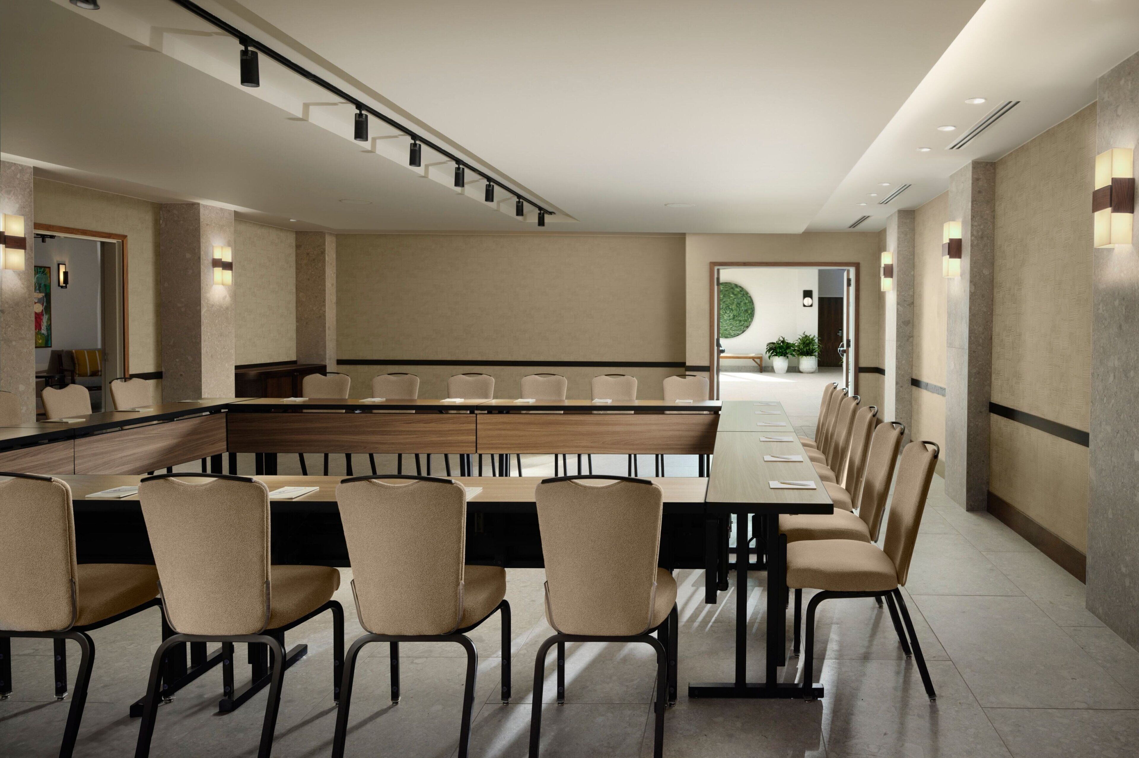 A modern conference room with a long table and chairs, recessed lighting, and a neutral color palette.
