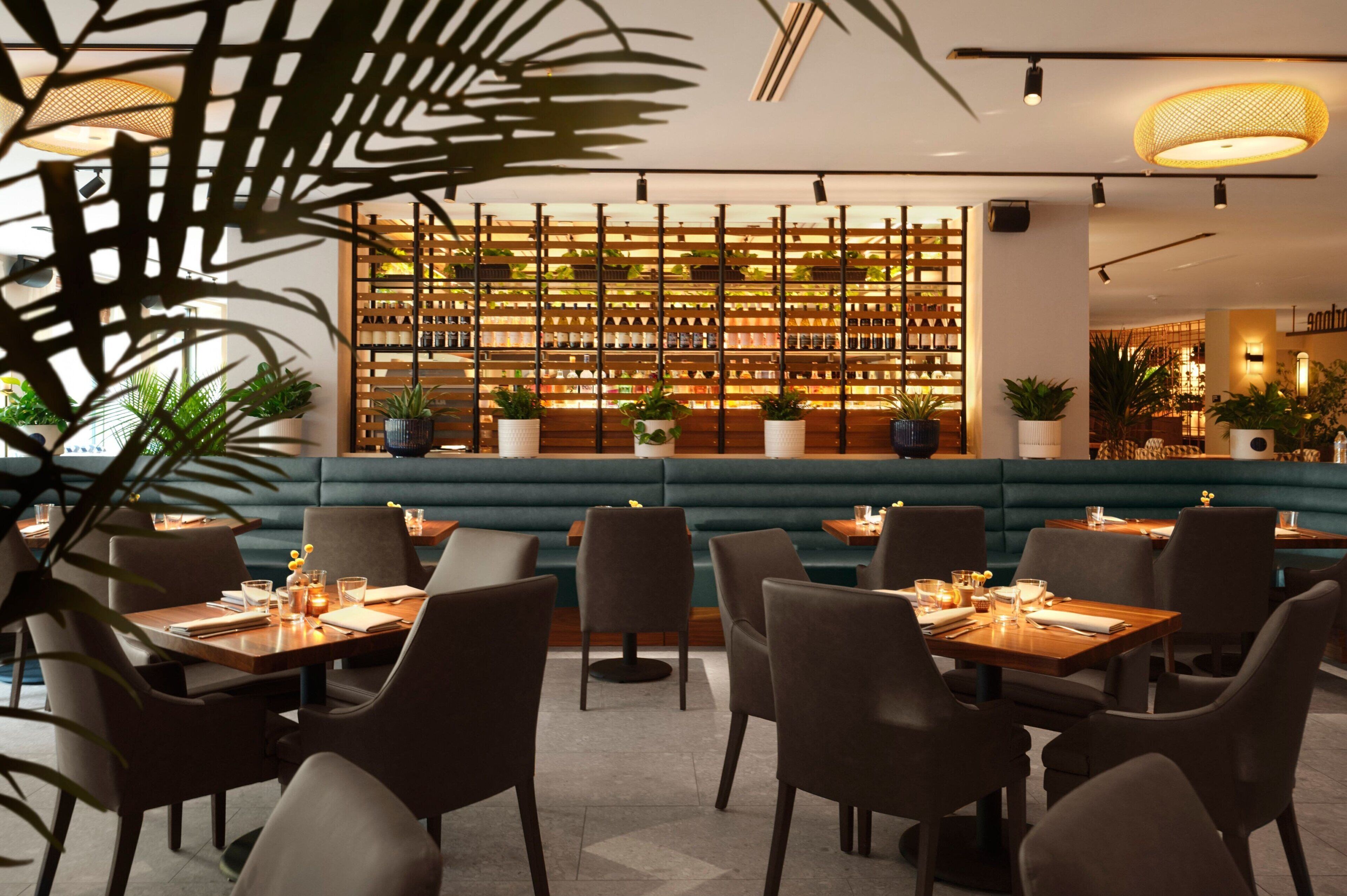 Un restaurant avec des banquettes, des tables et un mur végétal.
