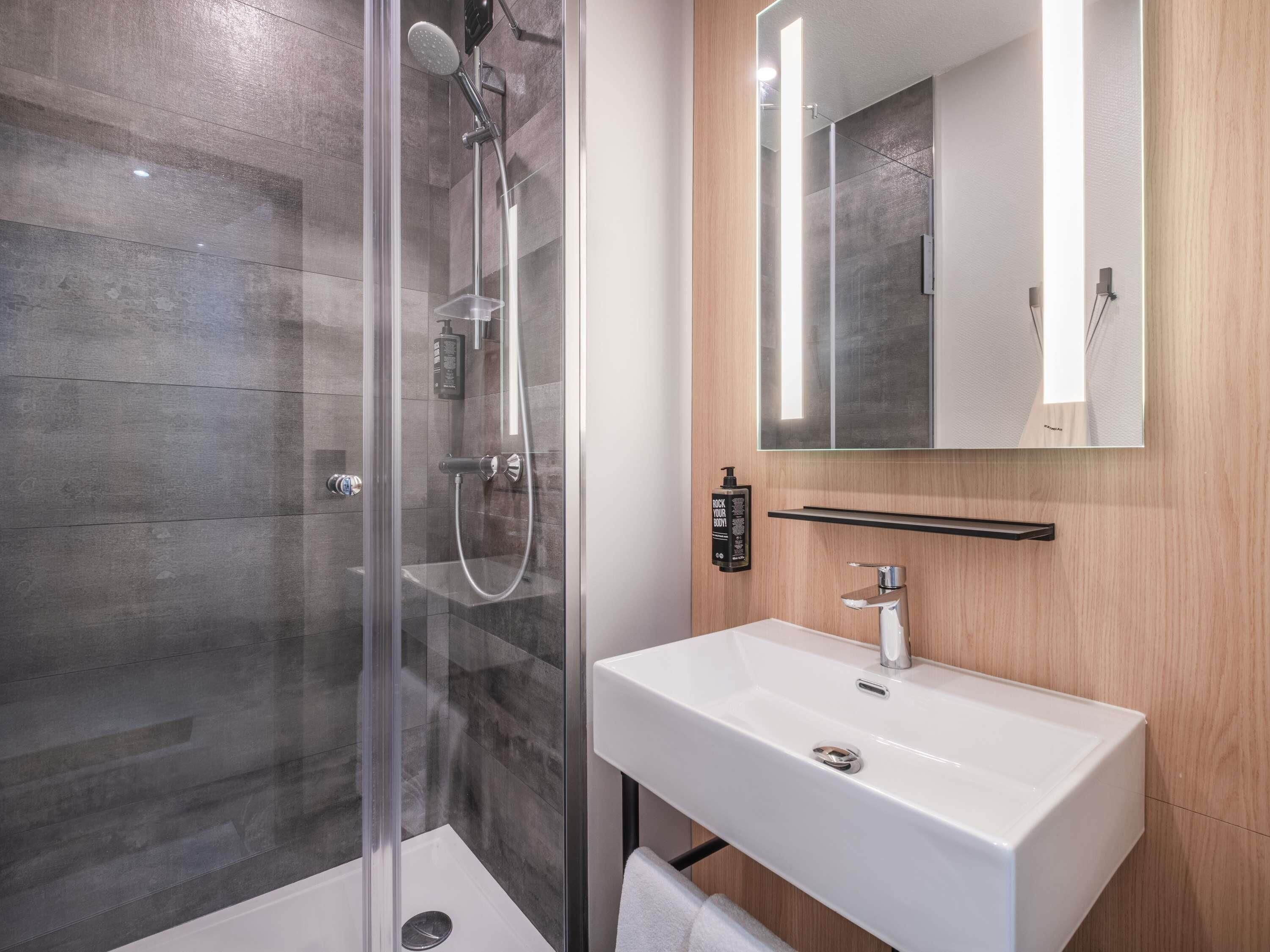 Un baño moderno con ducha de vidrio, lavamanos blanco y tocador de madera.