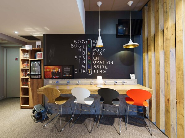 A modern workspace with a blackboard displaying business-related words, a water dispenser, and a seating area with chairs. - ibis Saint Quentin Basilique (Saint-Quentin)