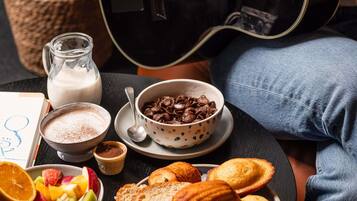 A breakfast setting with a guitar, a bowl of cereal, a glass of milk, and a plate of toast and pastries.