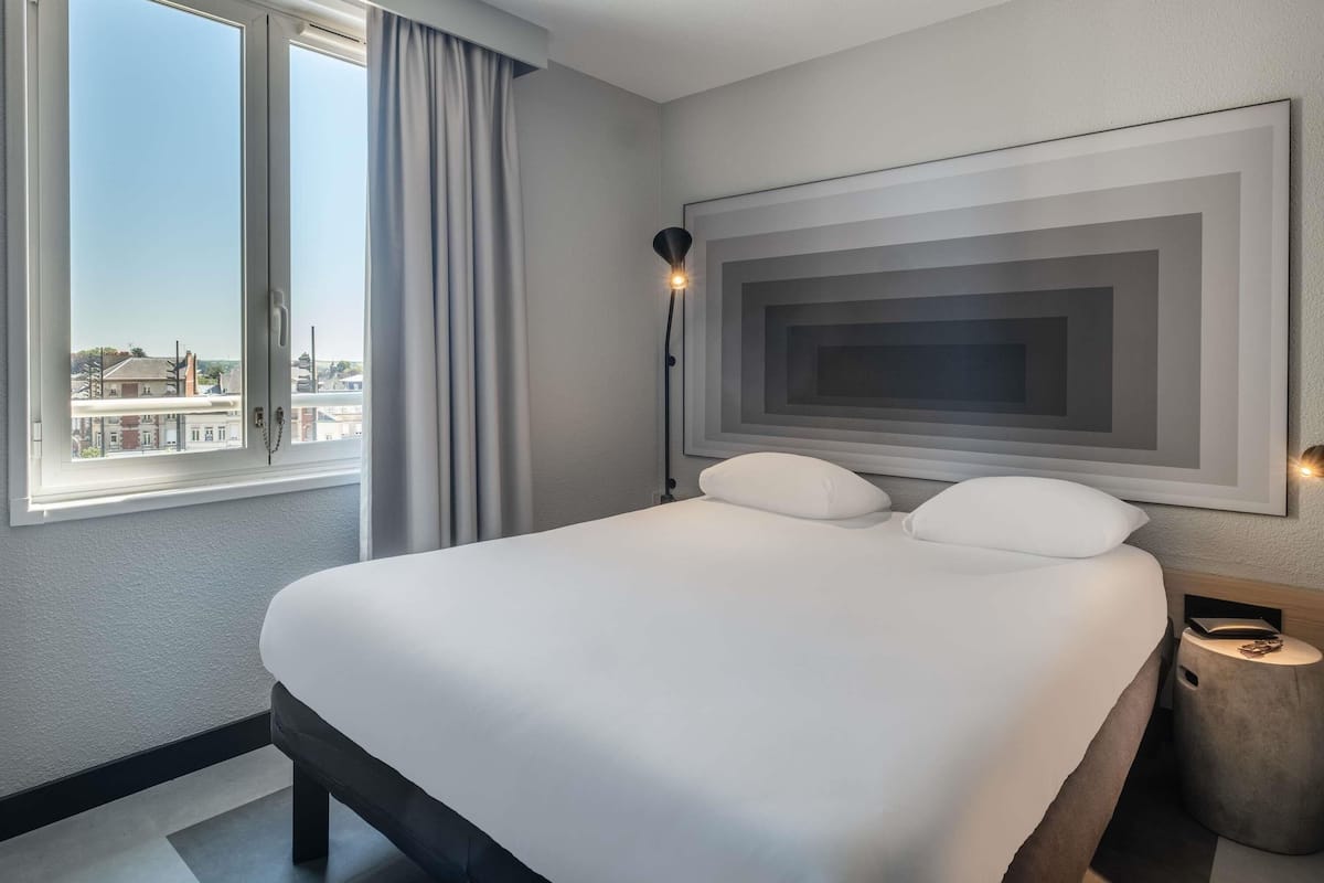 Quarto de hotel com uma cama grande, vista da cidade pela janela e uma obra de arte moderna na parede.