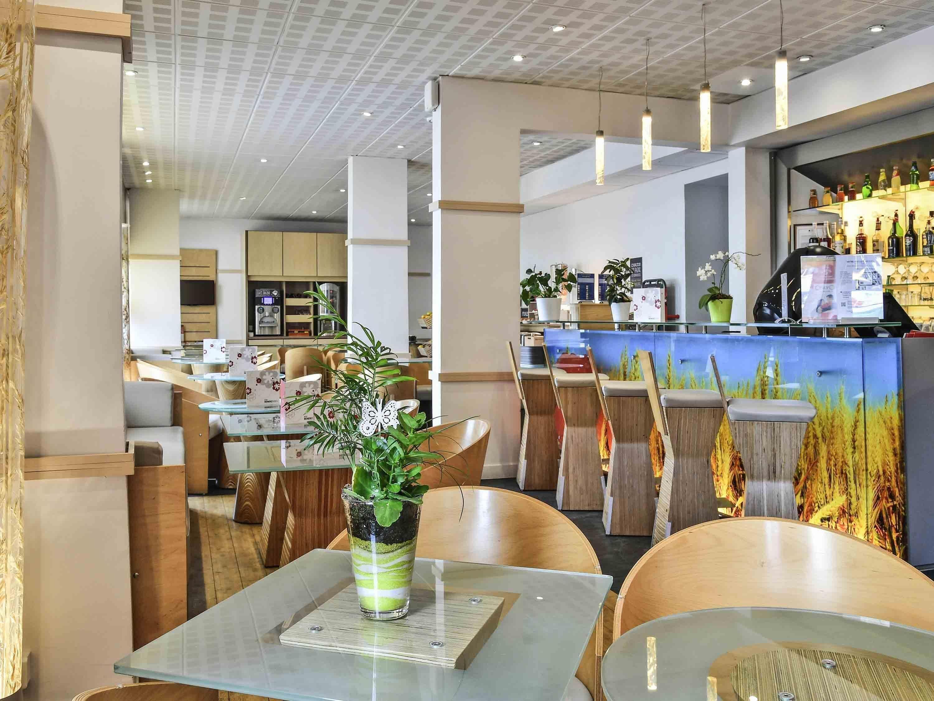 Interior moderno de un restaurante con barra, disposición de mesas y un centro de mesa decorativo con plantas.