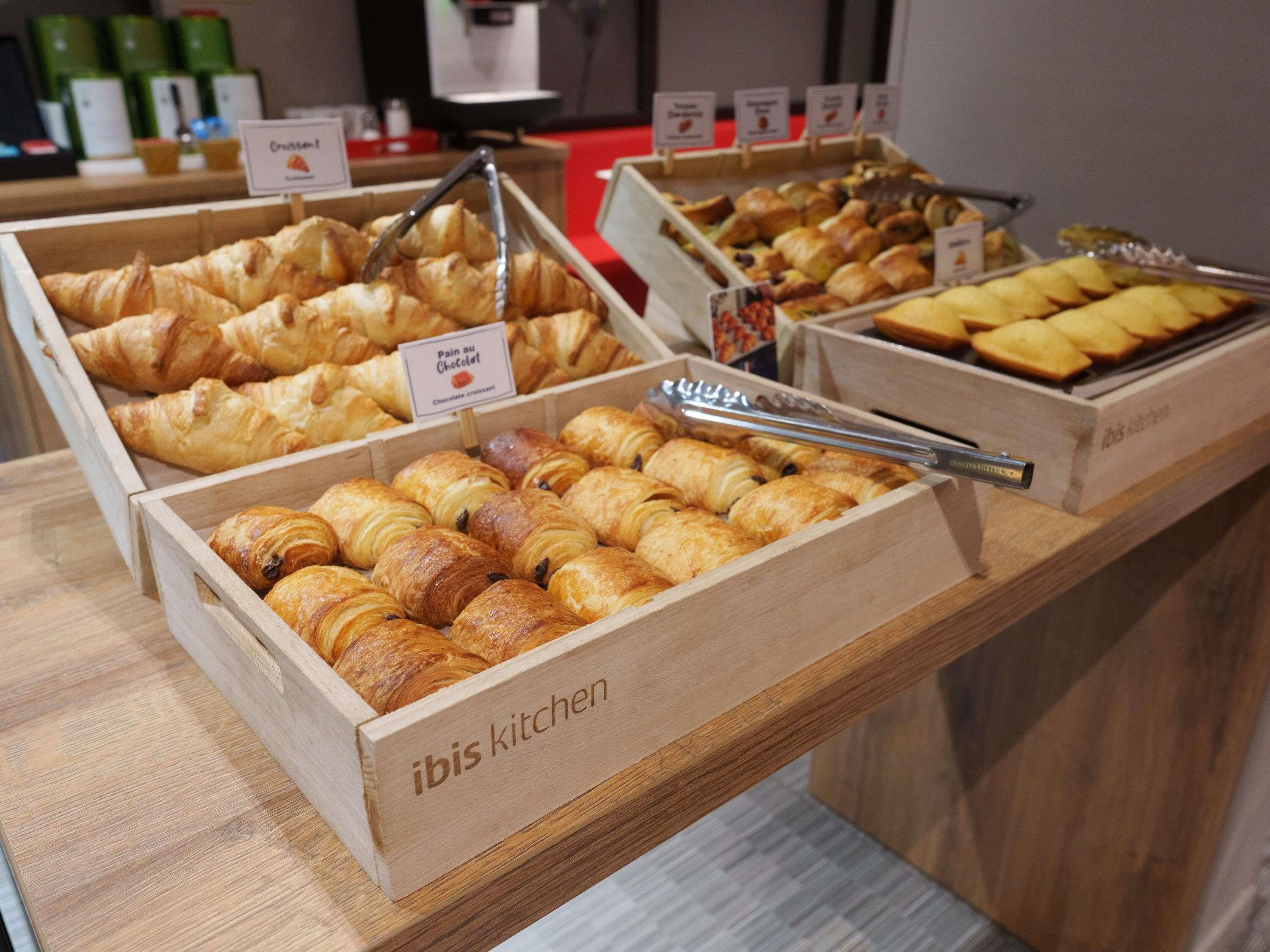 Una vetrina di pasticceria con diversi tipi di dolci, tra cui croissant e croissant al cioccolato, con etichette che riportano nomi come 'Pain au Chocolat' e 'Pain au Chocolat'.