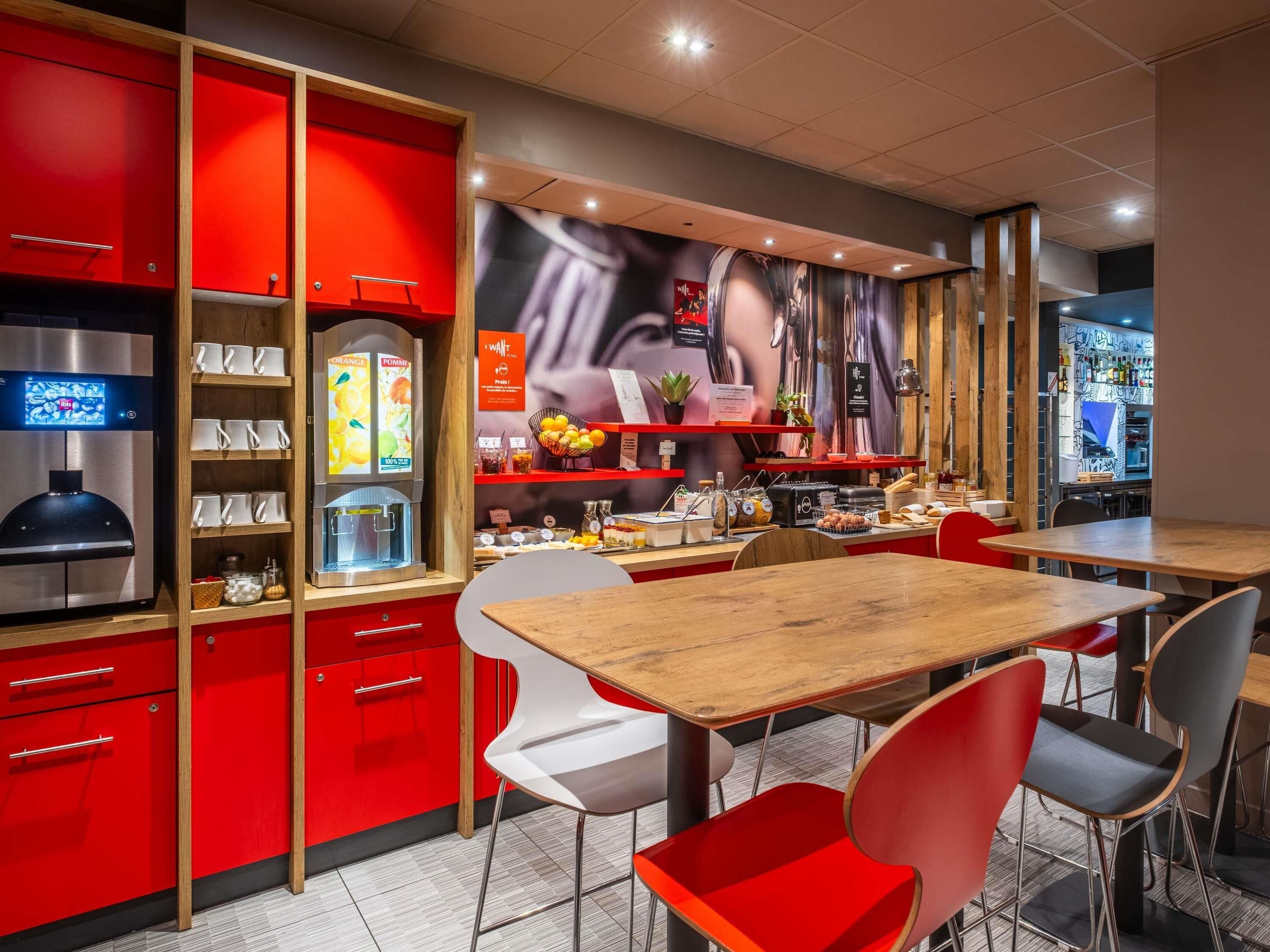 Een modern caféinterieur met rode kasten, een koffieapparaat en verschillende etenswaren in het zicht.