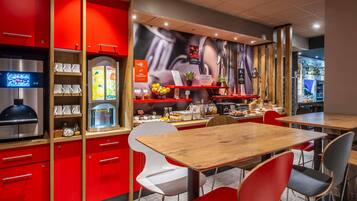 Een modern caféinterieur met rode kasten, een koffieapparaat en verschillende etenswaren in het zicht.