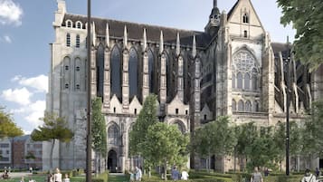 A historic cathedral with a large rose window and tall spires, surrounded by a well-maintained garden and a modern building in the background.